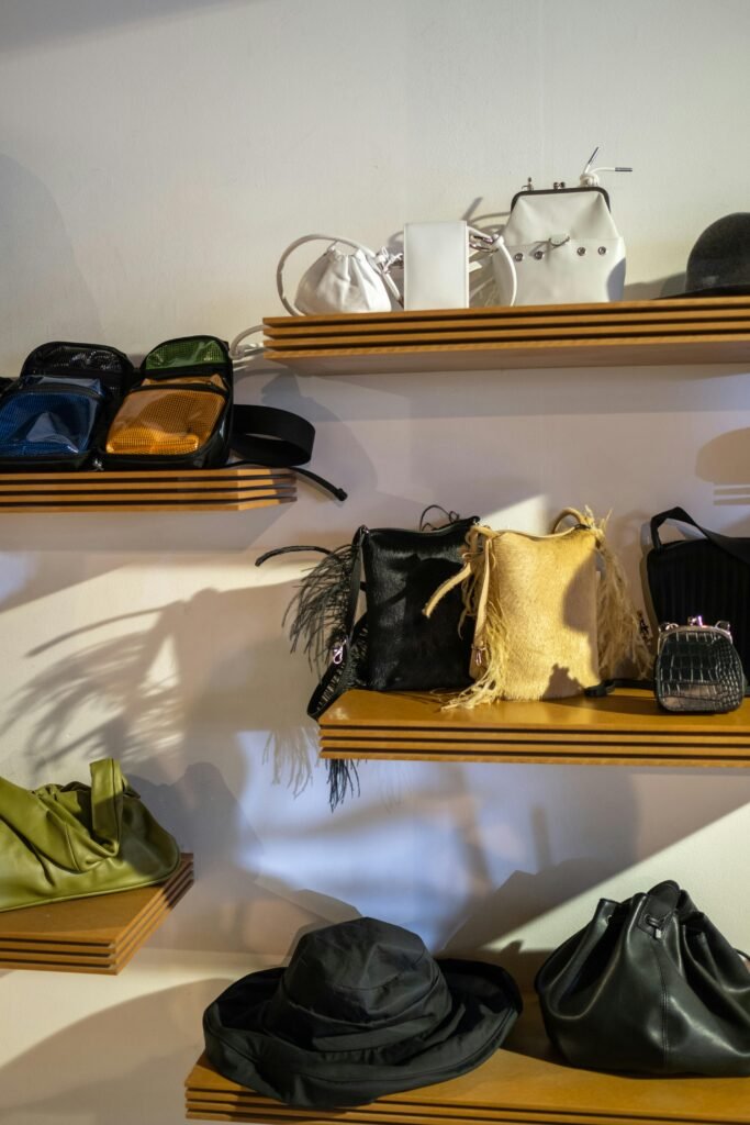 A collection of fashion bags and a hat displayed on wooden shelves in a boutique setting.